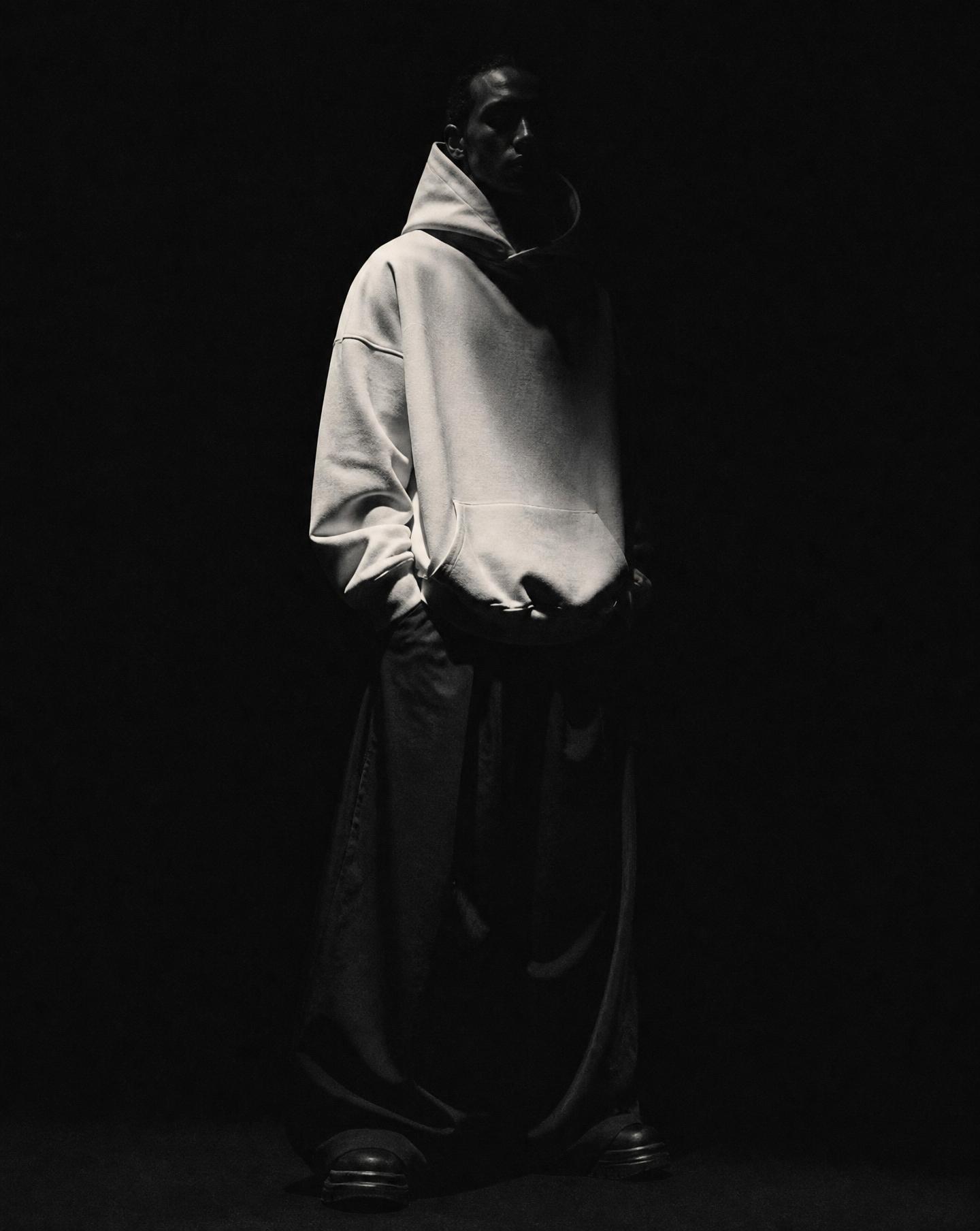 Figure in an oversized bone hoodie emerging from darkness